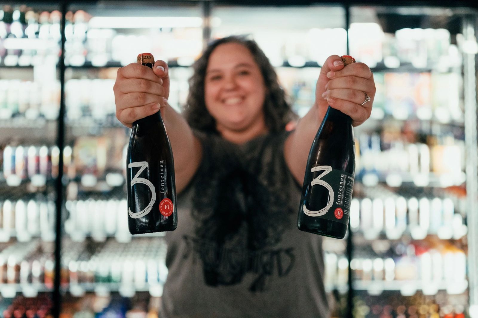 Staff member holding up two bottles of beer in front of the coolers